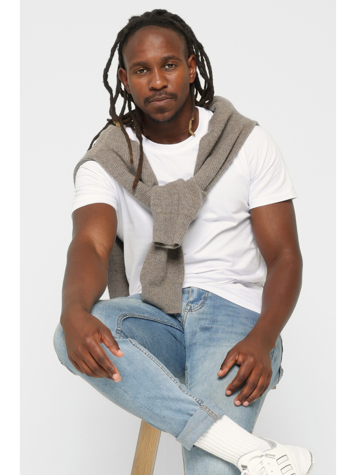 Man wearing a gray sweater over a premium cotton white t-shirt with blue jeans on a white background