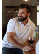 Man sitting at a table with a glass of red wine, wearing a white premium cotton polo shirt.