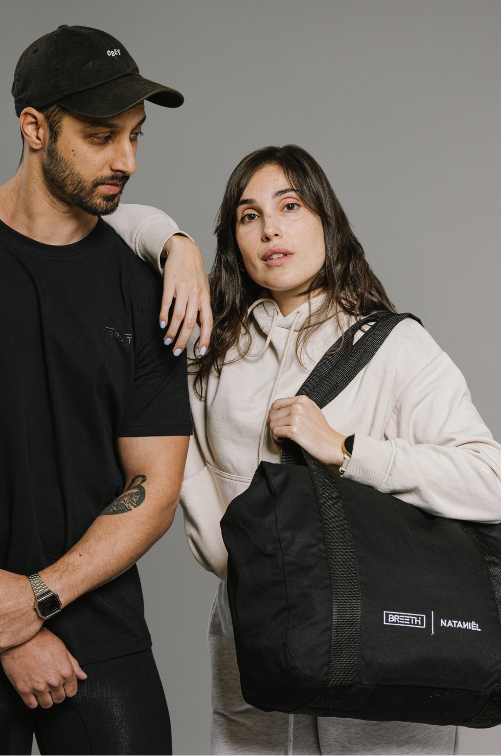 Man and woman standing together with a black bag, wearing branded clothing.