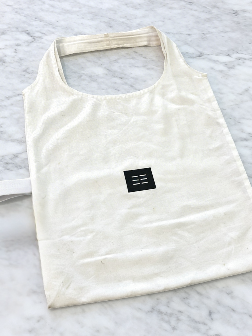 White reusable bag with a black logo on a light gray marble background. Eco-friendly reusable cotton shopper bag in South Africa