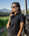 Woman in a black cotton polo shirt made from Oeko-Tex fabric in South Africa by BREETH. Breathable cotton golf shirt designed for comfort, durability, and a clean, everyday look. Wearing sunglasses standing next to a vehicle with a scenic background